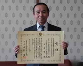 表彰された男性が賞状を持っている写真